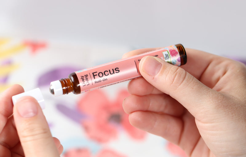 Two hands in the forefront of the image. the background is blurred. the hands are holding the "Focus" roll on bottle from Lively Living