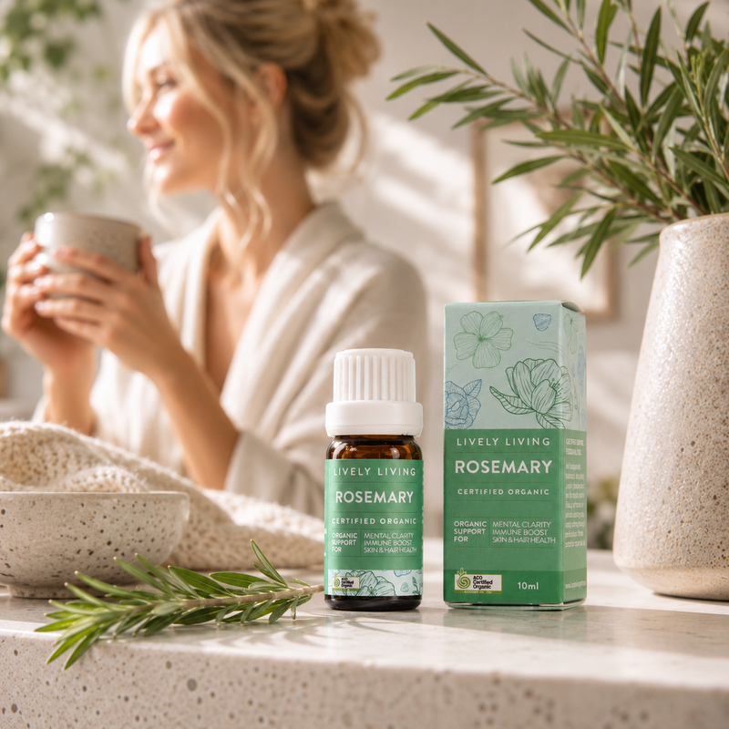 Woman in a bathrobe holding a mug with Lively Living Rosemary essential oil bottle and packaging on a table.