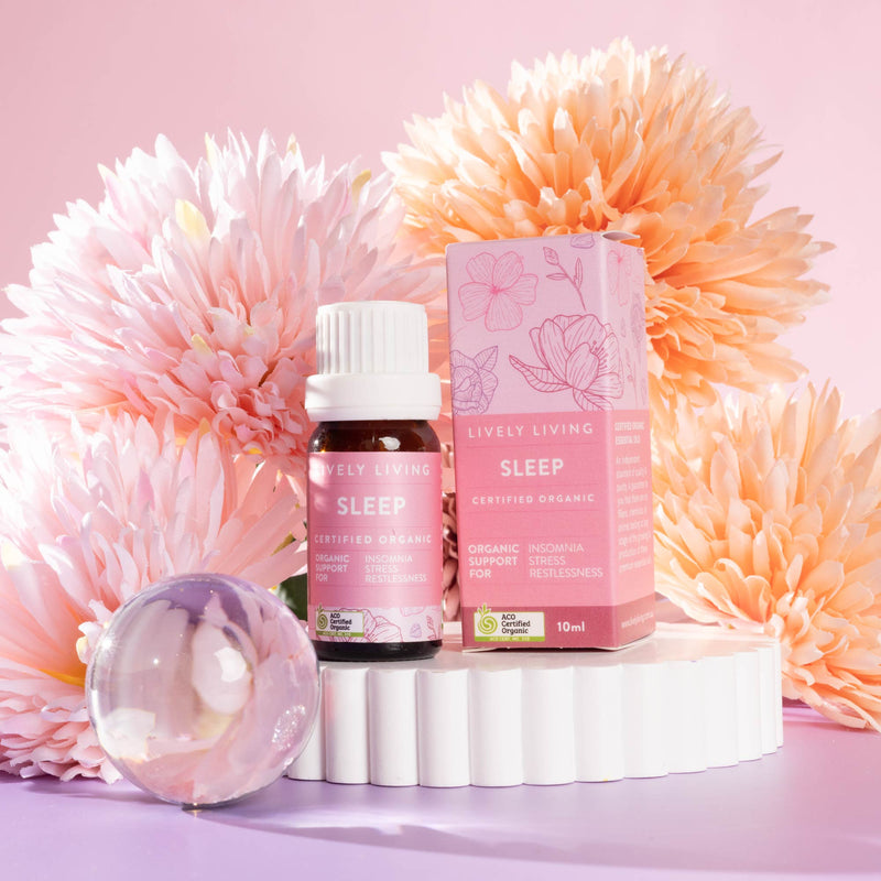 Lively Living "sleep" essential oil bottle sitting on a white rippled plinth surrounded by pink and orange flowers on a pink background