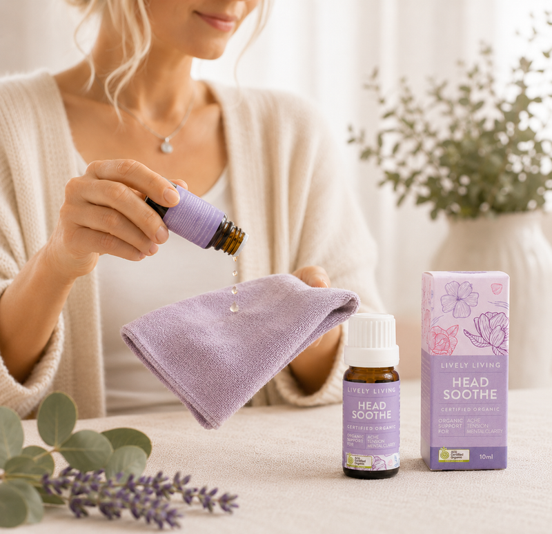 Woman holding a purple bottle of 'Head Soothe' essential oil with a matching towel and packaging on a light surface.