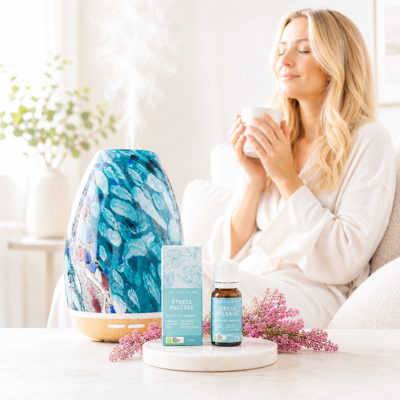 Woman holding a mug with a diffuser, essential oil bottle, and packaging on a table.