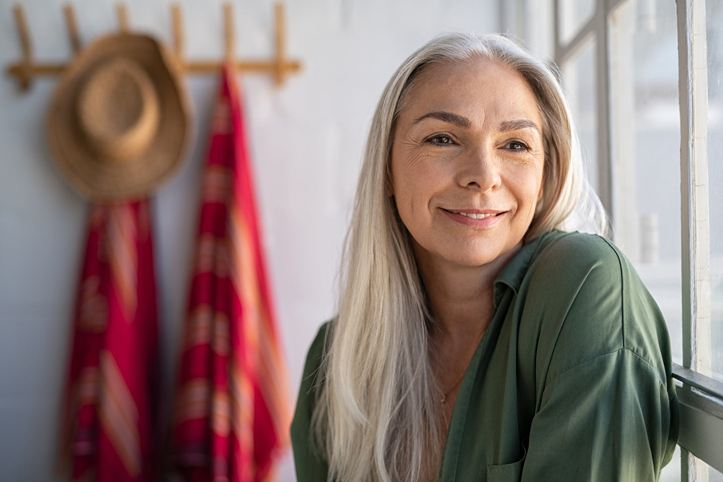 Smiling woman with long silver hair in a green shirt at home