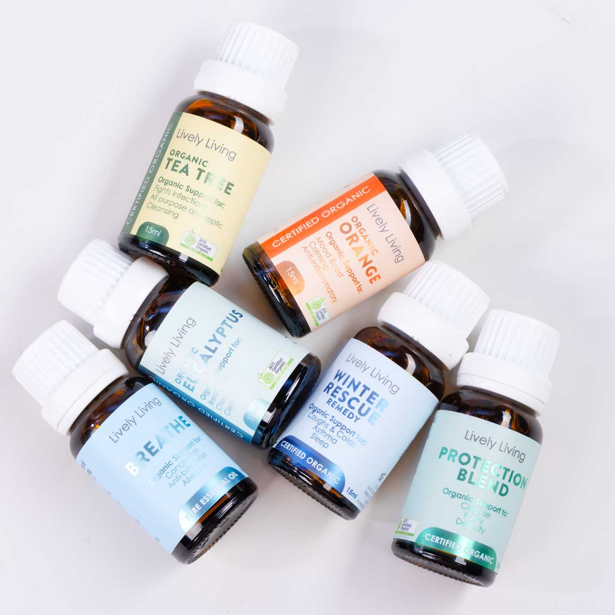 Six small amber glass supplement bottles with white caps from Lively Living, arranged on a clean white background. The bottles include Organic Tea Tree, Certified Organic Orange, Allyria, Winter Rescue, Protection Blend, and Breath Support.