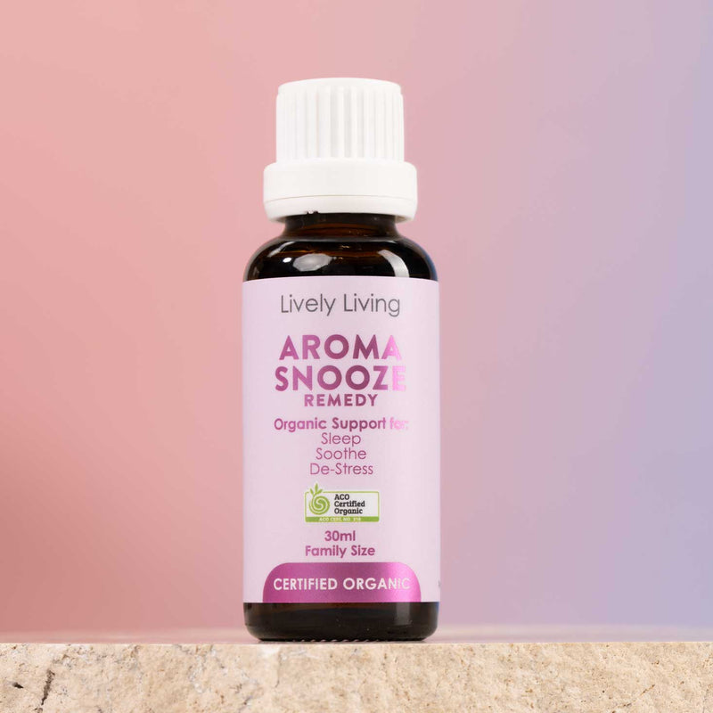 A 30ml bottle of Lively Living 'Aroma Sneeze Remedy' organic support oil, featuring a white cap and a light pink label, set against a soft pink and purple gradient background.
