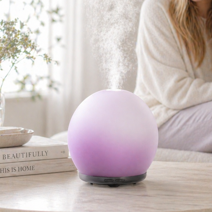 Woman sitting on a couch with a purple lamp on a table in a bright living room.