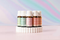 Lively Living essential oils on white rippled stand, including "grapefruit, hush little baby, mandarin, sniffles and chest, spearmint" on a rainbow background