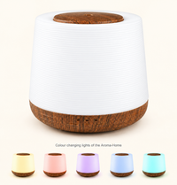 Aroma-Home diffuser with a ribbed white body and wood-look base and lid, with five small versions showing its colour changing lights in warm white, pink, lilac, blue and aqua