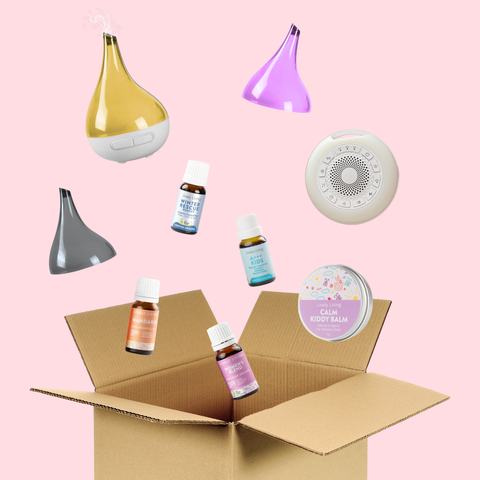 Collection of diffusers and essential oil bottles with a cardboard box on a pink background