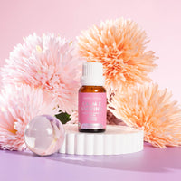 Lively Living "calm and unwindi" essential oil bottle sitting on a white rippled plinth surrounded by pink and orange flowers on a pink background