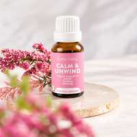 Lively Living Calm & Unwind certified organic essential oil bottle with a pink label on a round stone coaster, with pink heather flowers in the foreground