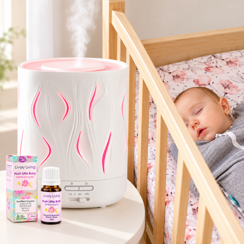 A white and pink Lively Living humidifier with a baby bottle and box next to a wooden crib where a sleeping baby rests.