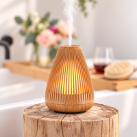 Wood-look Aroma-Flare Diffuser with slatted fins glowing warm amber and releasing mist on a timber stump beside a bath, with pink roses, a glass of red wine and a bath brush on a bath tray