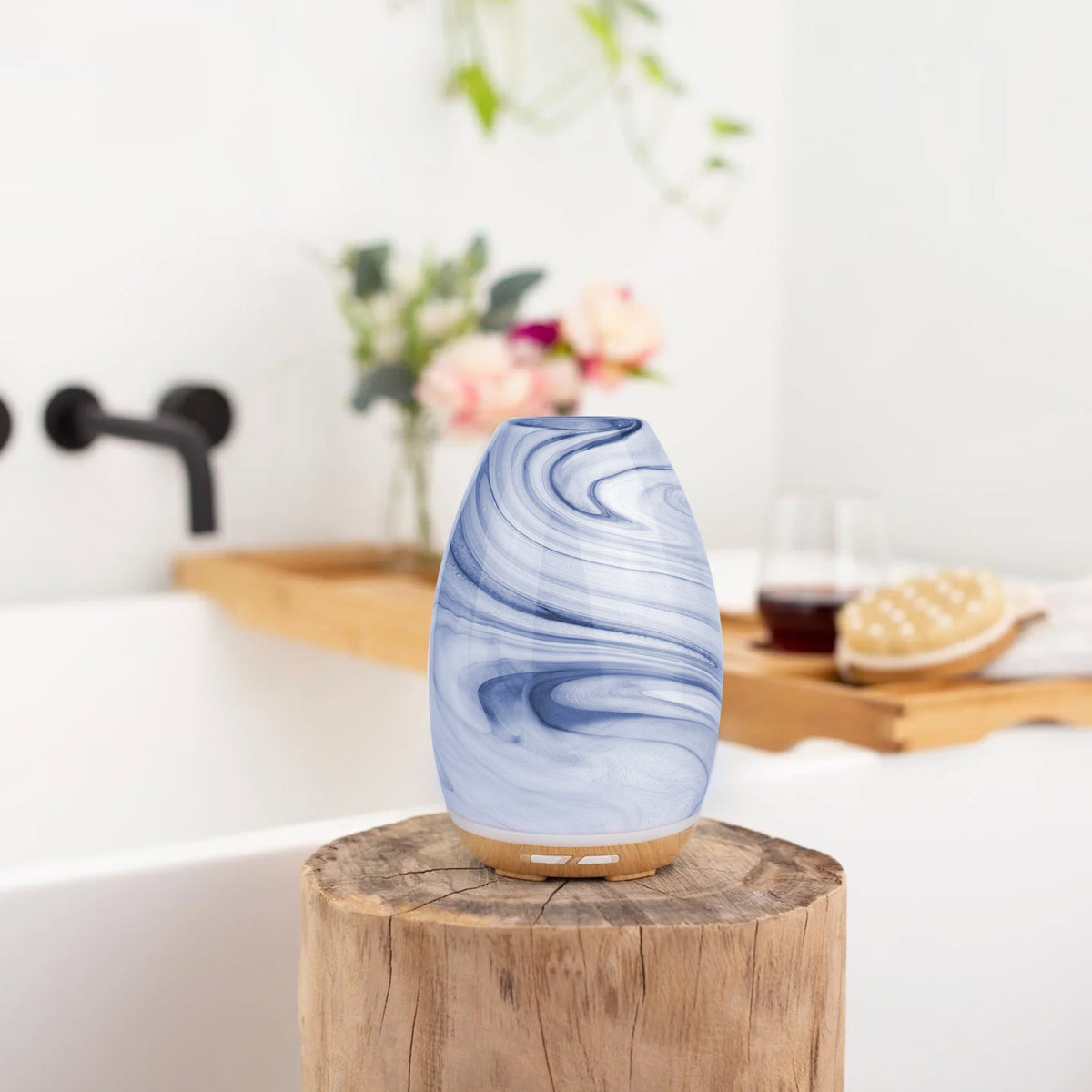 Blue marbled diffuser on a wooden block with a bathtub and flowers in the background