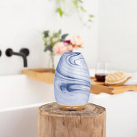 Blue marbled diffuser on a wooden block with a bathtub and flowers in the background