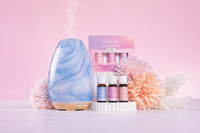 Marbled blue and beige diffuser with essential oil bottles and packaging on a pink background