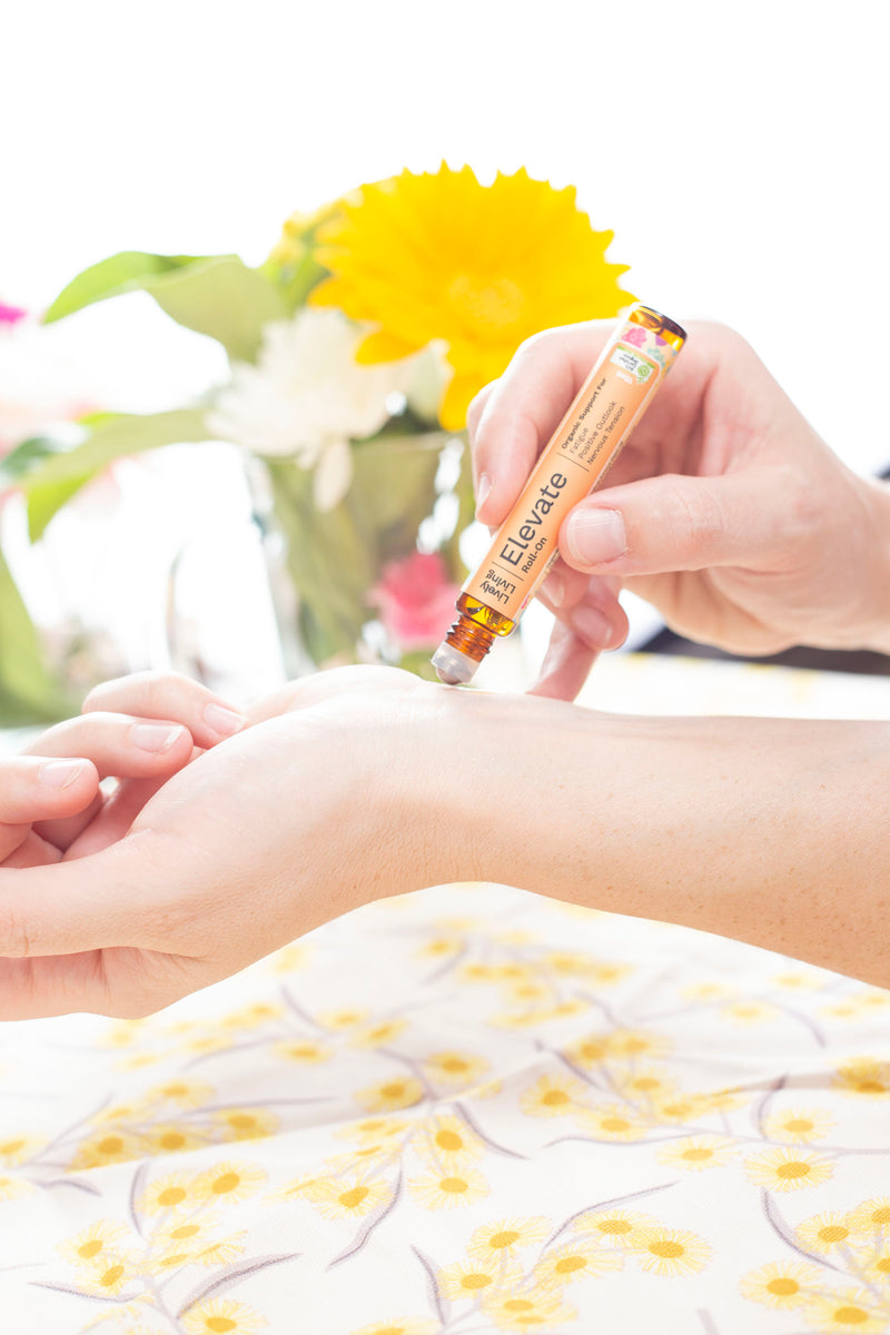 Hand applying a roll-on product to a wrist with flowers in the background