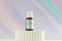 The Lively Living "Eucalyptus" essential oil bottle with a green logo siting on a rippled white plinth with a rainbow purple background