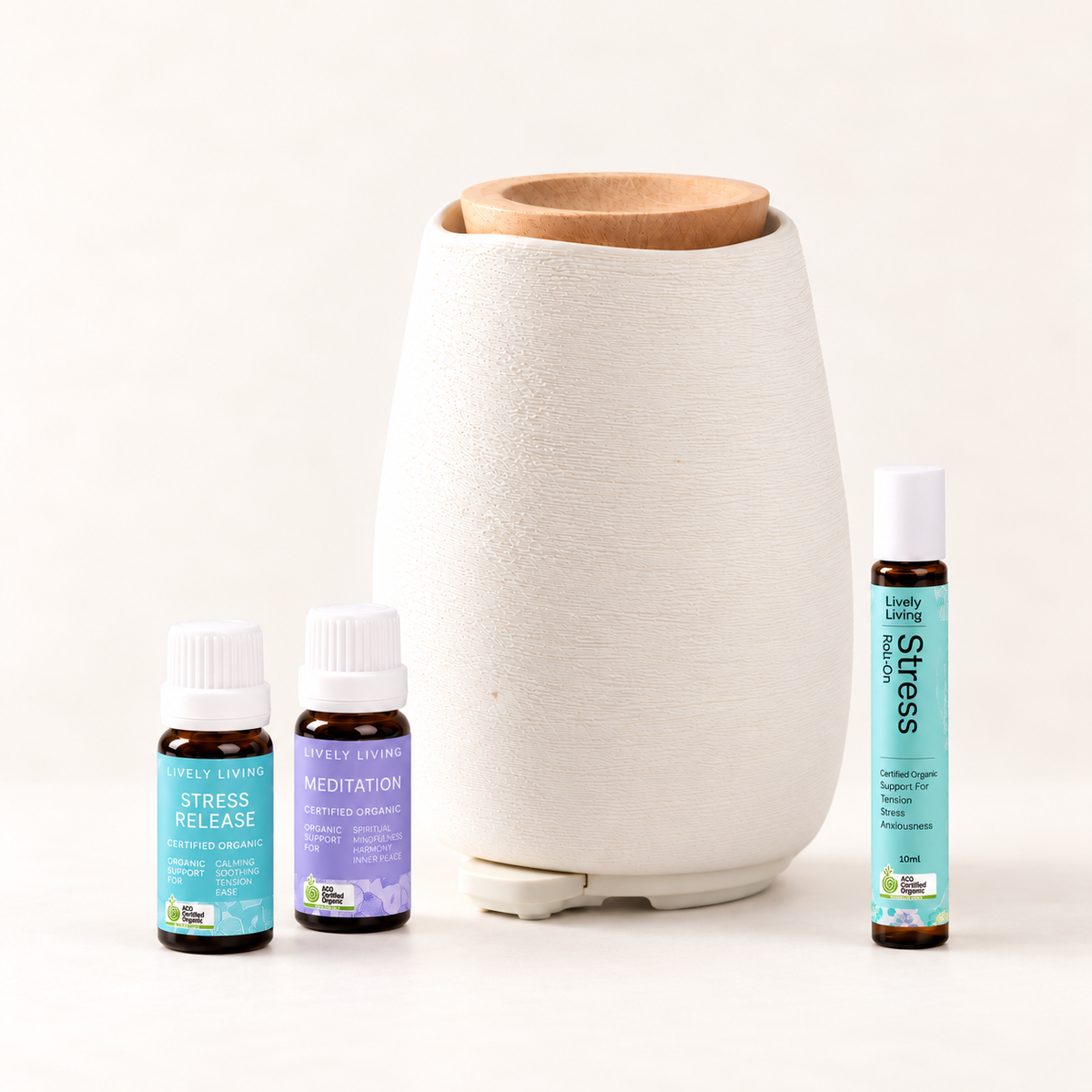 White ceramic Aroma-Fern diffuser with a bamboo lid beside Lively Living Stress Release and Meditation oils and a Stress roll-on, from the Aroma-Fern Calm Starter Set