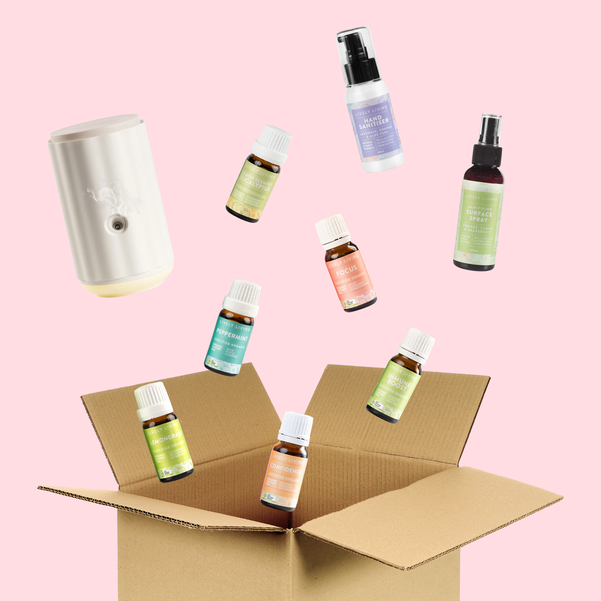 Open cardboard box with essential oil bottles and a diffuser on a pink background