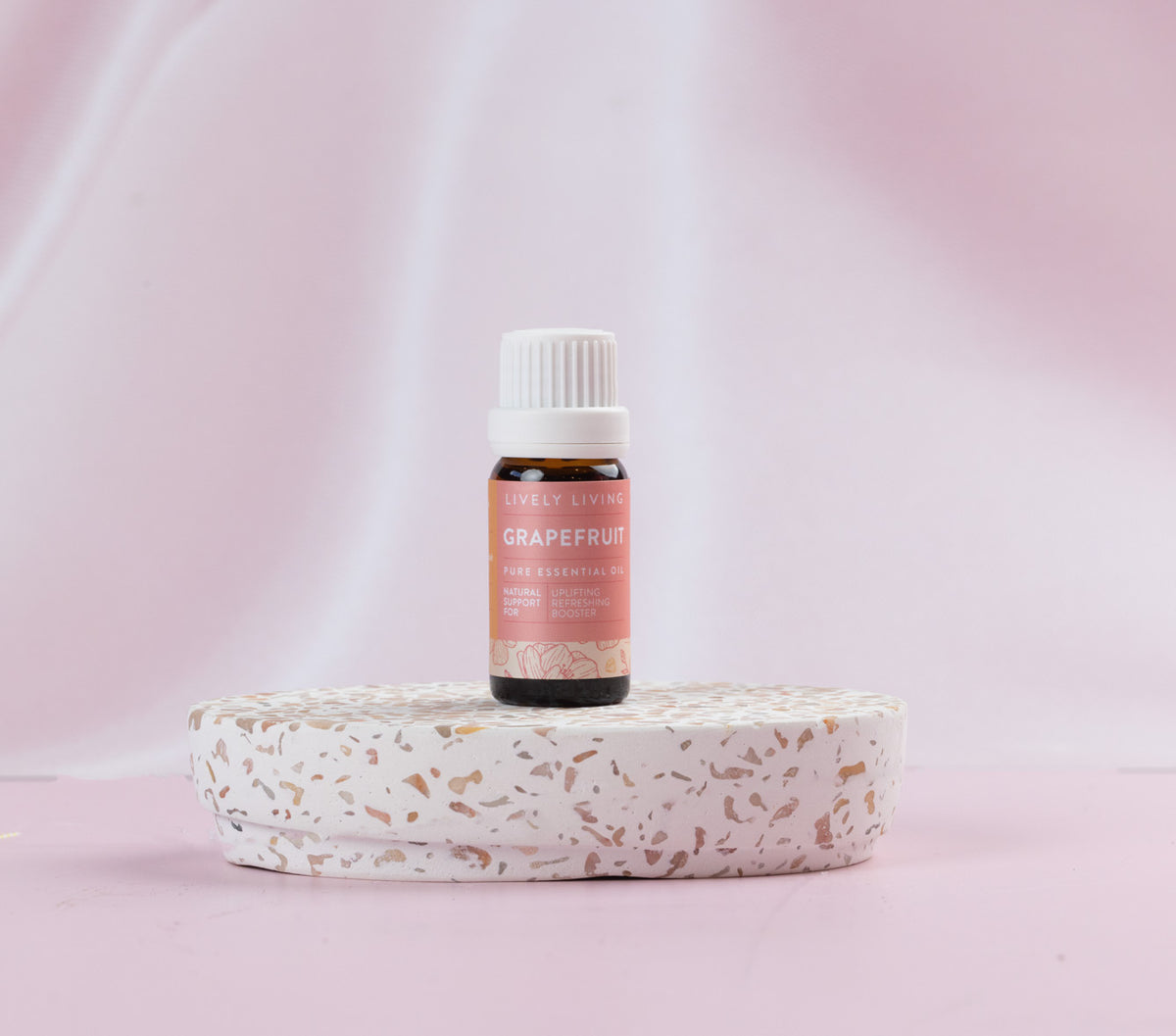 Lively Living essential Grapefruit oil is sitting on  terrazzo platform wit a light pink background. 