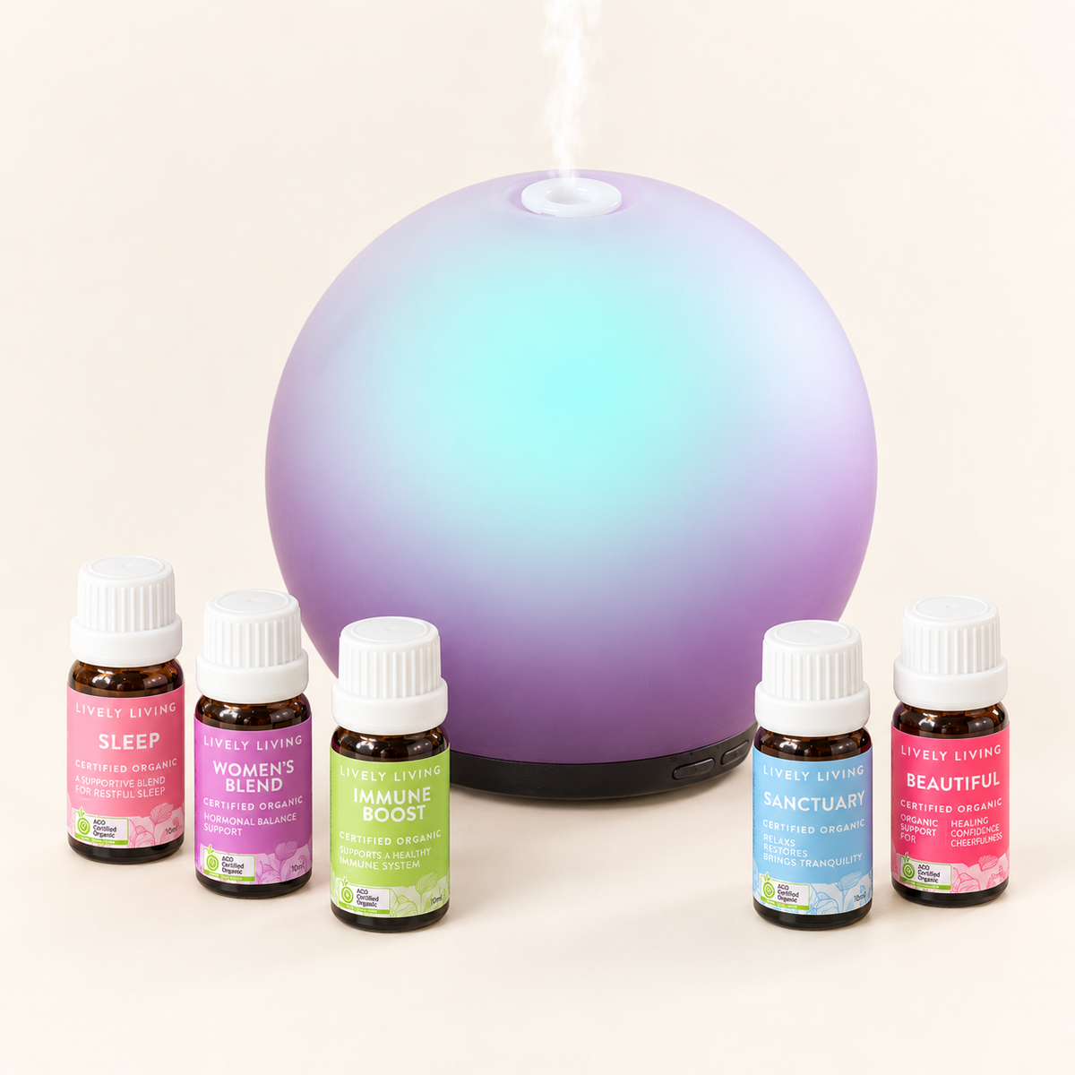 Aroma-Halo Glass Diffuser in iridescent mauve with an aqua glow, releasing mist behind five Lively Living certified organic oils: Sleep, Women's Blend, Immune Boost, Sanctuary and Beautiful