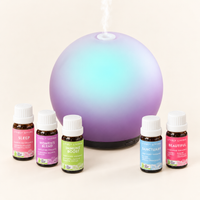 Aroma-Halo Glass Diffuser in iridescent mauve with an aqua glow, releasing mist behind five Lively Living certified organic oils: Sleep, Women's Blend, Immune Boost, Sanctuary and Beautiful