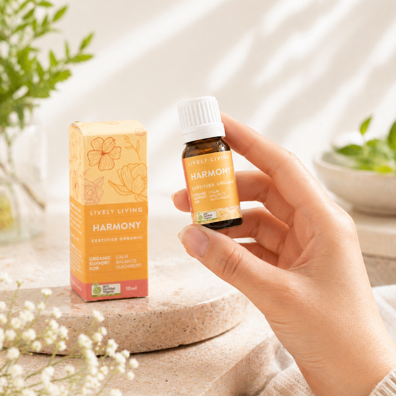 Hand holding a bottle of Lively Living Harmony essential oil with packaging in the background.