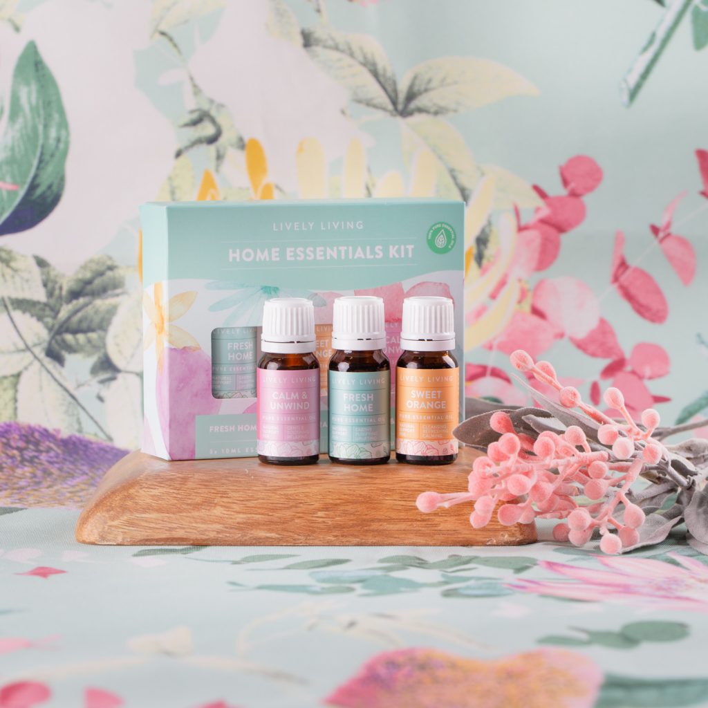Lively Living trio home essentials oils, Calm unwind, fresh home and sweet orange. sitting on front of the Lively Living kit pack and on a floral background