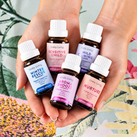 Two hands holding five Lively Living certified organic oils, Winter Rescue, Sensitive Child, Child Calming, Aroma Snooze and Nurture, over a botanical print fabric