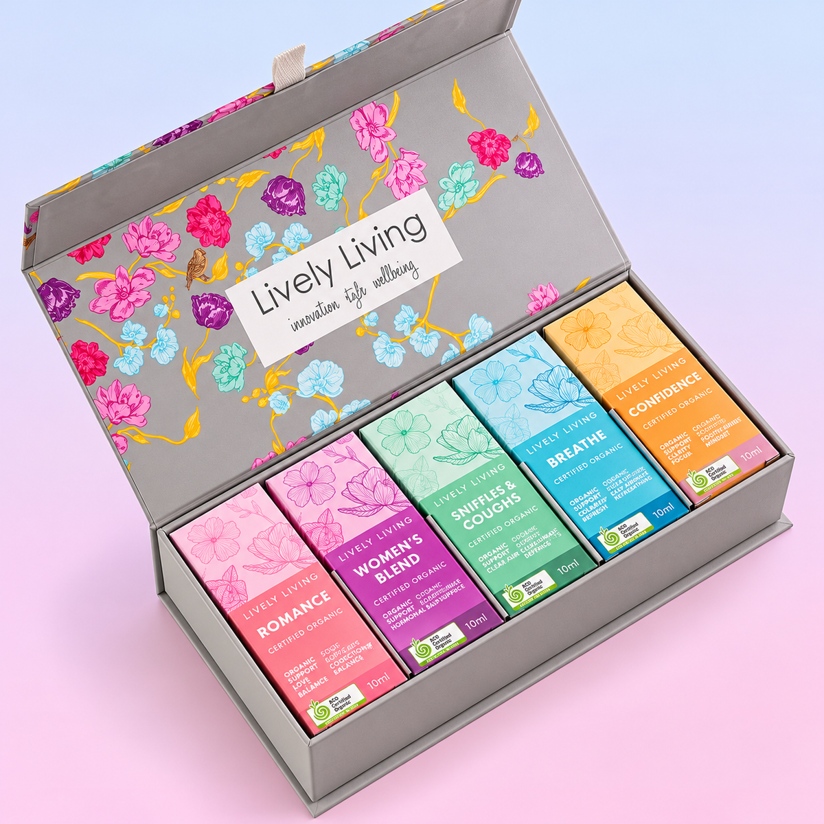 Open grey Lively Living floral gift box holding five essential oil boxes including Romance, Women's Blend and Breathe, on a pastel pink and blue background