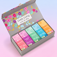 Open grey Lively Living floral gift box holding five essential oil boxes including Romance, Women's Blend and Breathe, on a pastel pink and blue background