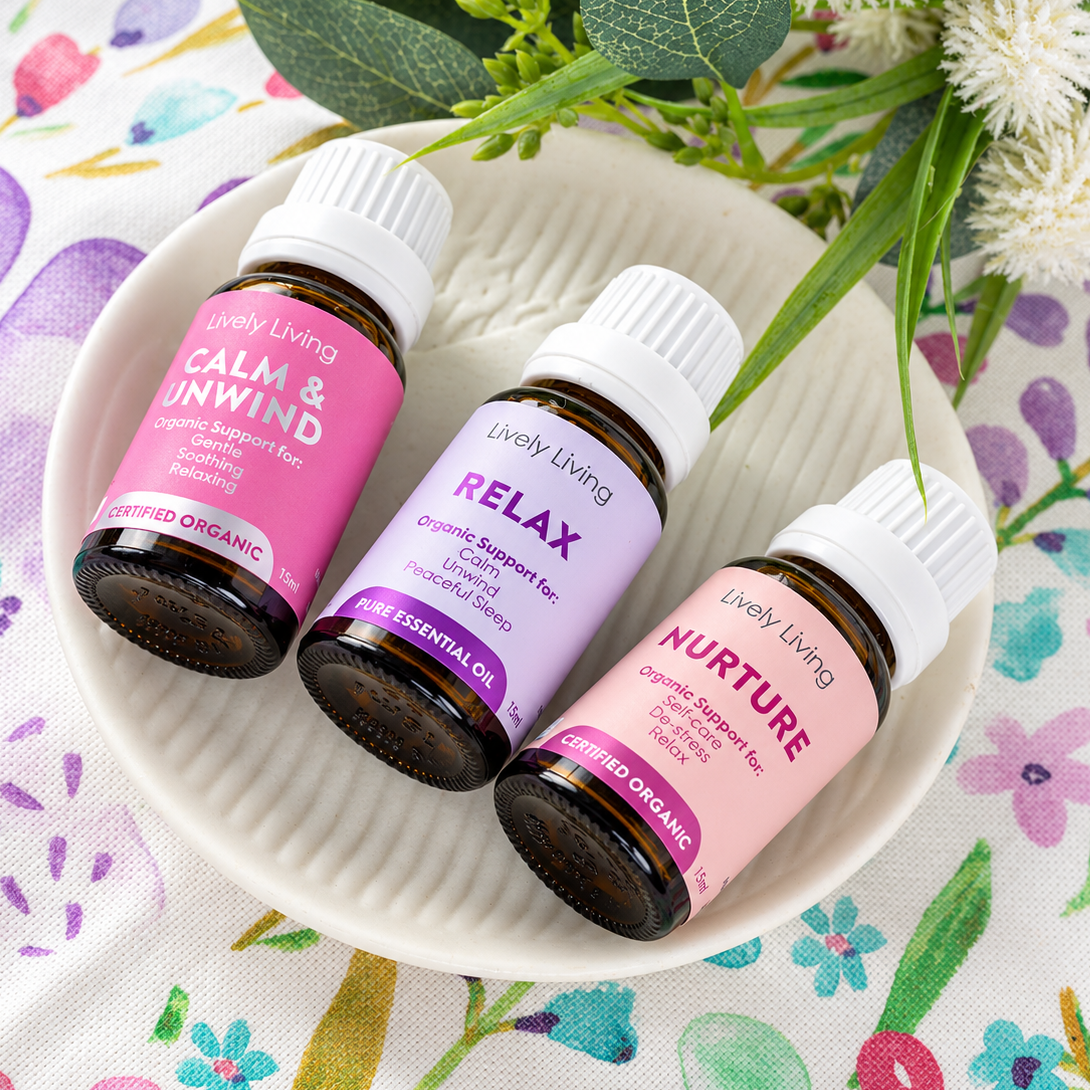 Lively Living Calm & Unwind, Relax and Nurture essential oil bottles lying on a white ceramic dish on a watercolour floral cloth with white flowers and greenery