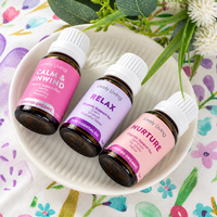 Lively Living Calm & Unwind, Relax and Nurture essential oil bottles lying on a white ceramic dish on a watercolour floral cloth with white flowers and greenery