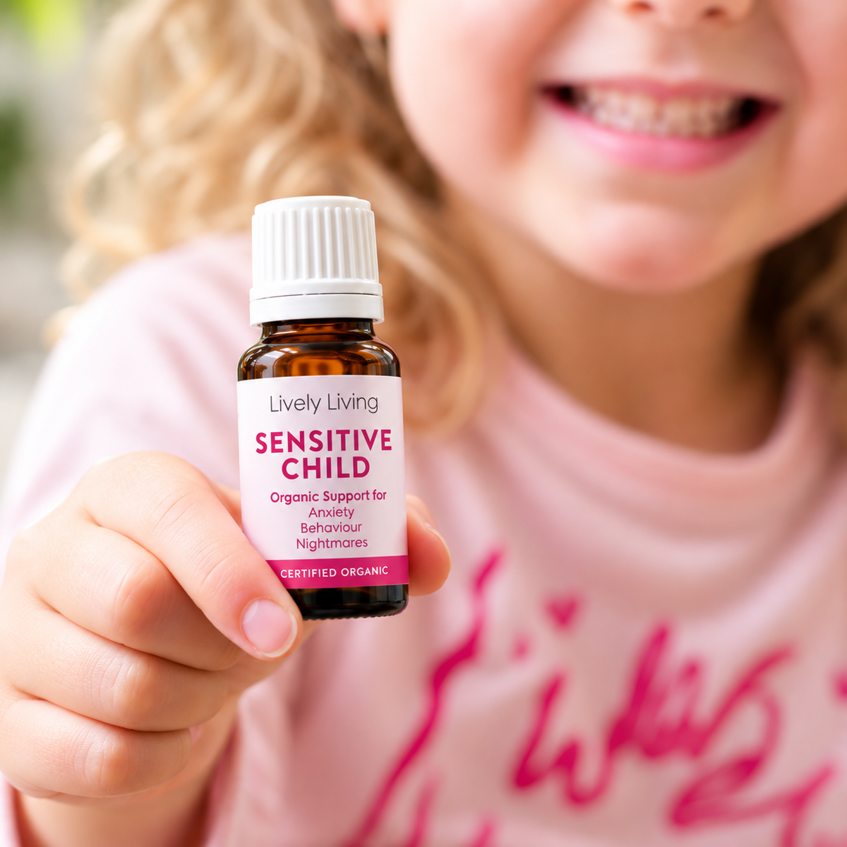 Smiling young girl holding up a Sensitive Child essential oil bottle