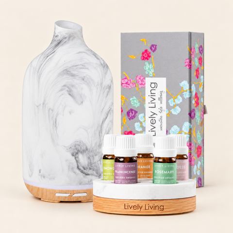 Aroma-Dune Grey Marle diffuser on a wood-look base beside five Lively Living certified organic oils on a round stand and the floral gift box