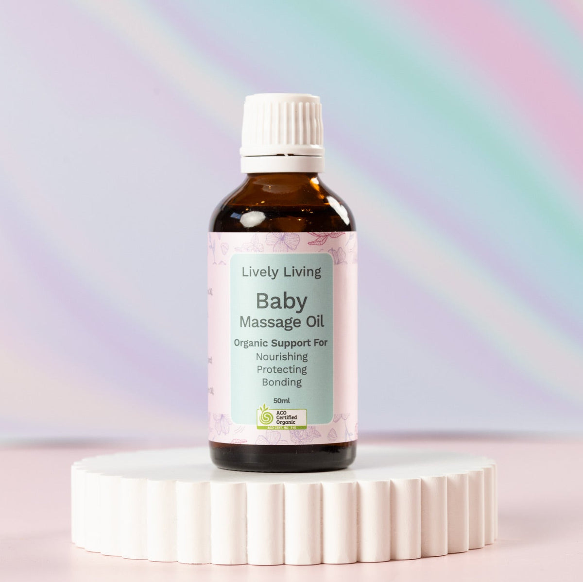 Baby Massage Oil Organic Lively Living, sitting on a rippled white base, with a multi coloured background