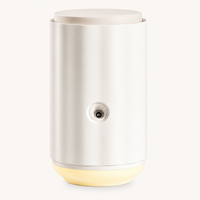 White cylindrical diffuser with a small round outlet on the front and a soft warm light at the base, on a cream background