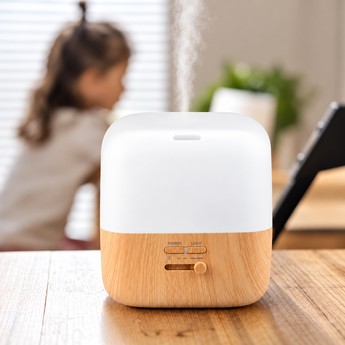 A compact tabletop humidifier with a white top section and a light wood-grain bottom base sits on a wooden table. Steam is visibly rising from the top, and a blurred child and indoor room are in the background.