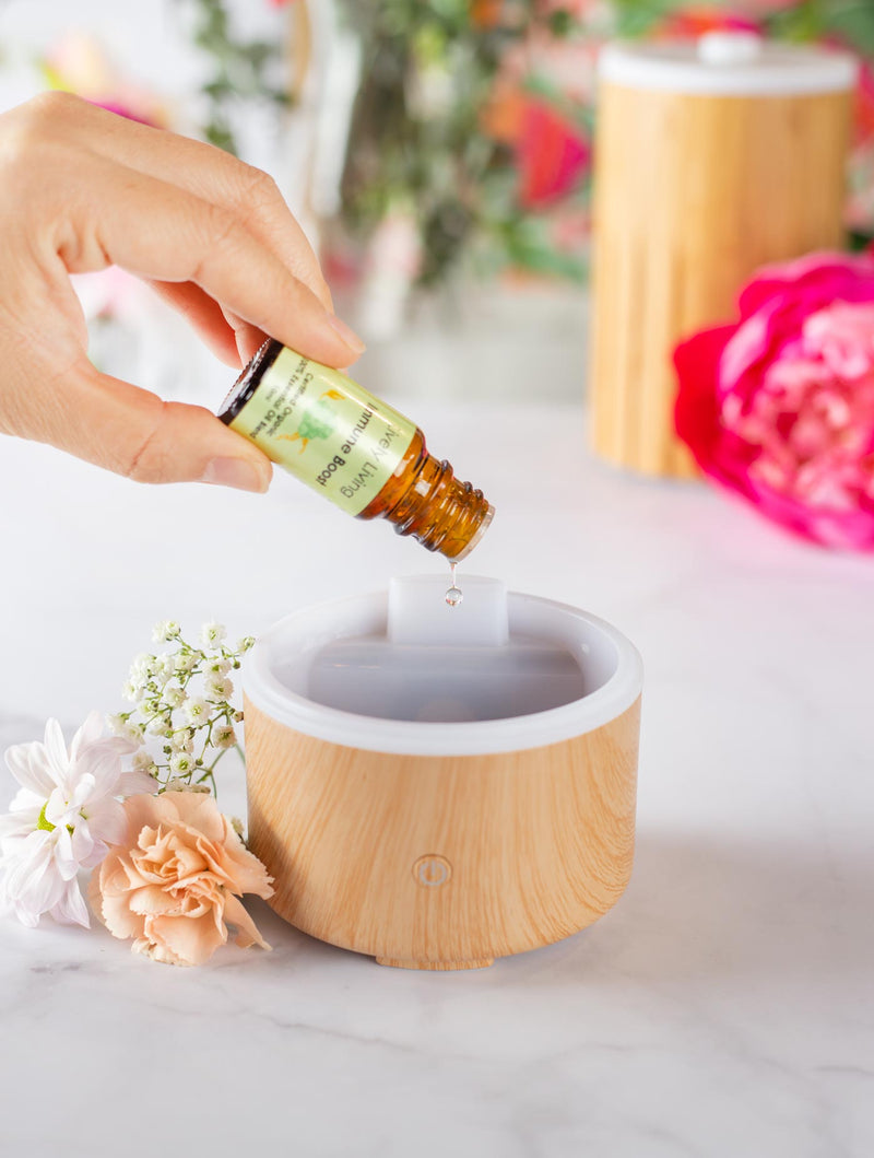 Hand adding essential oil to a diffuser with flowers in the background