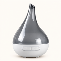 A modern teardrop-shaped essential oil diffuser with a translucent dark gray upper chamber and a white base featuring two control buttons, shown on a clean off-white background.