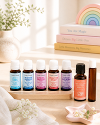 Collection of essential oil bottles on a wooden tray with a rainbow decoration in the background.