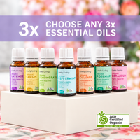 Six small amber essential oil bottles with white caps are displayed on a white pedestal. Above them, a purple banner reads '3x CHOOSE ANY 3x ESSENTIAL OILS.