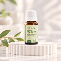 Lively Living Organic Tea Tree 15ml essential oil with a green label on a white fluted pedestal, with a sprig of green leaves beside it