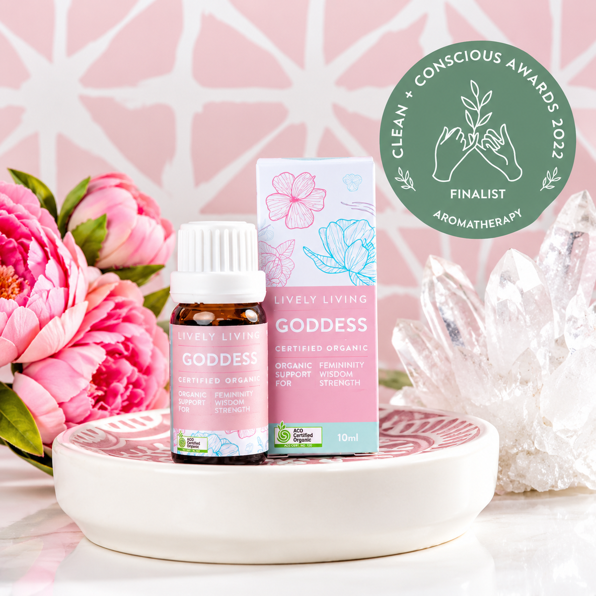 Goddess certified organic essential oil and box on a ceramic dish with pink peonies and quartz crystals, with a Clean + Conscious Awards 2022 Finalist badge