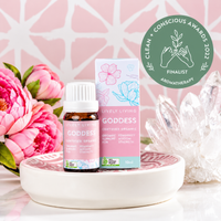 Goddess certified organic essential oil and box on a ceramic dish with pink peonies and quartz crystals, with a Clean + Conscious Awards 2022 Finalist badge