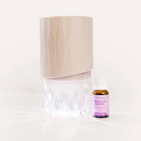 Clear diffuser with beige top and a small bottle labeled 'Indulge Blend' on a white background