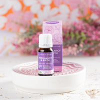 Lively Living "pregnancy and birth" essential oil with purple branding and box placed behind the bottle. sitting on a white plate and florals in the background
