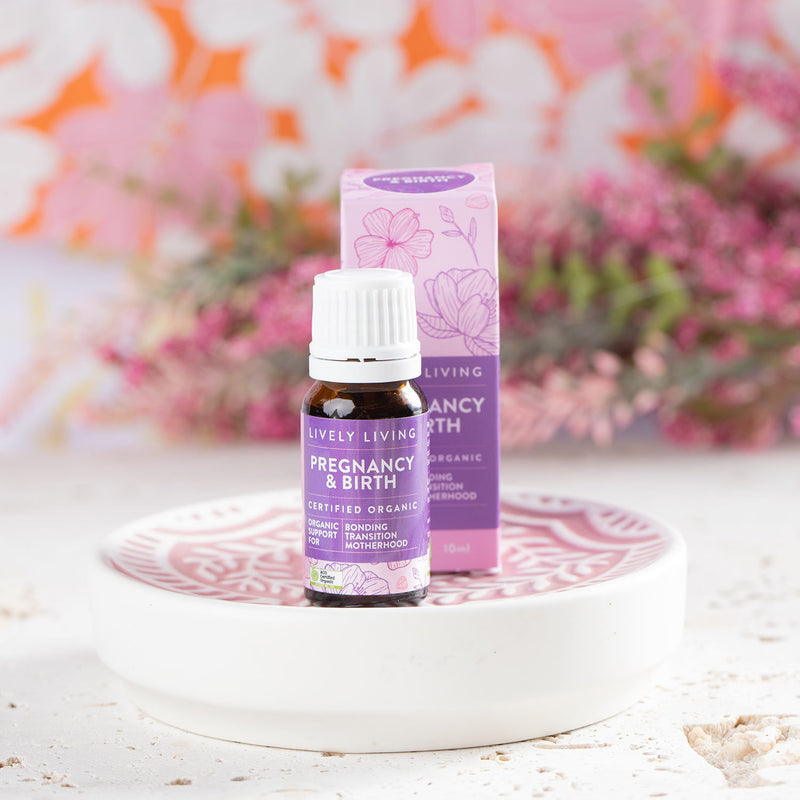 Lively Living "pregnancy and birth" essential oil with purple branding and box placed behind the bottle. sitting on a white plate and florals in the background