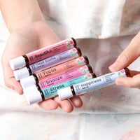 Two hands holding six Lively Living roll-ons including Focus, Snooze and Happiness