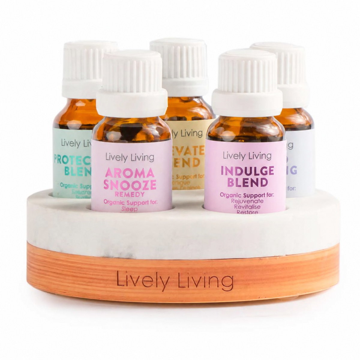 A set of five amber glass essential oil bottles with white ribbed caps, arranged on a round marble-and-wood display base. The front bottle has a pink label reading 'Lively Living Aroma Snooze,' with other visible labels including 'Protective Blend,' 'Private Blend,' and 'Indulge Blend.